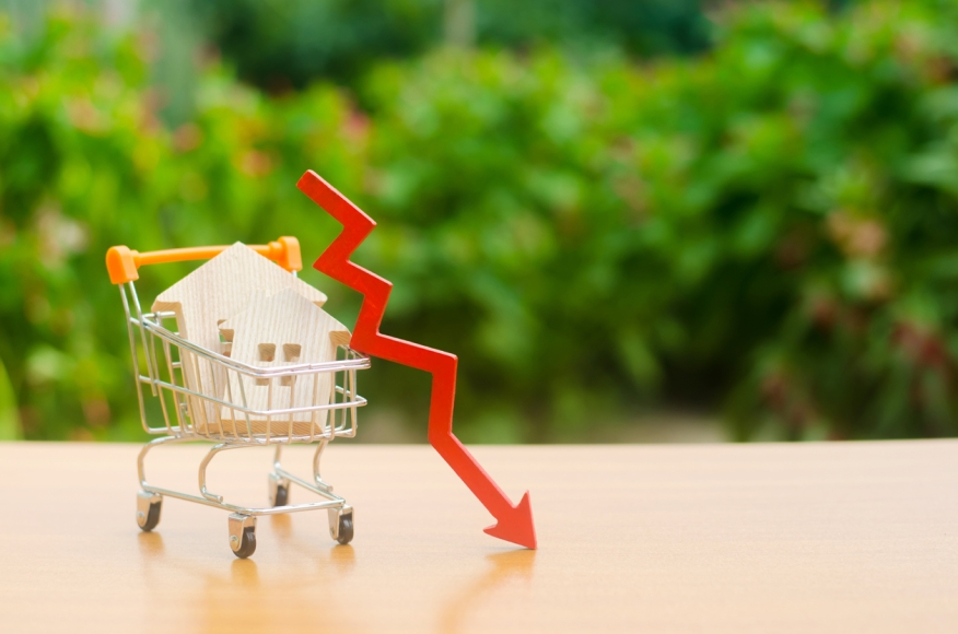 Wooden house in shopping cart and downward arrow. Photo credit: iStock.com/Andrii Yalanskyi