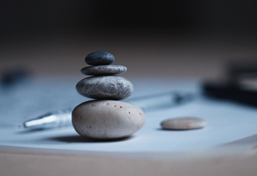 Rocks balancing on a desk next to a paper and pen.