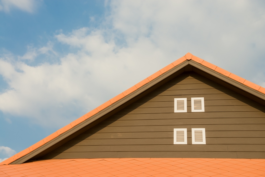 Orange and gray roof under blue sky with white clouds. 