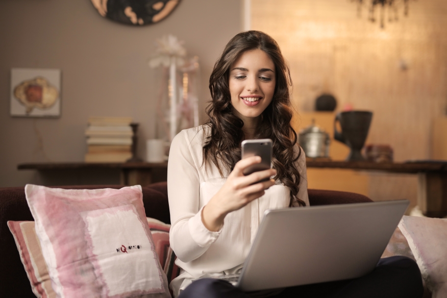 Woman shopping for a home using her cell phone and laptop.