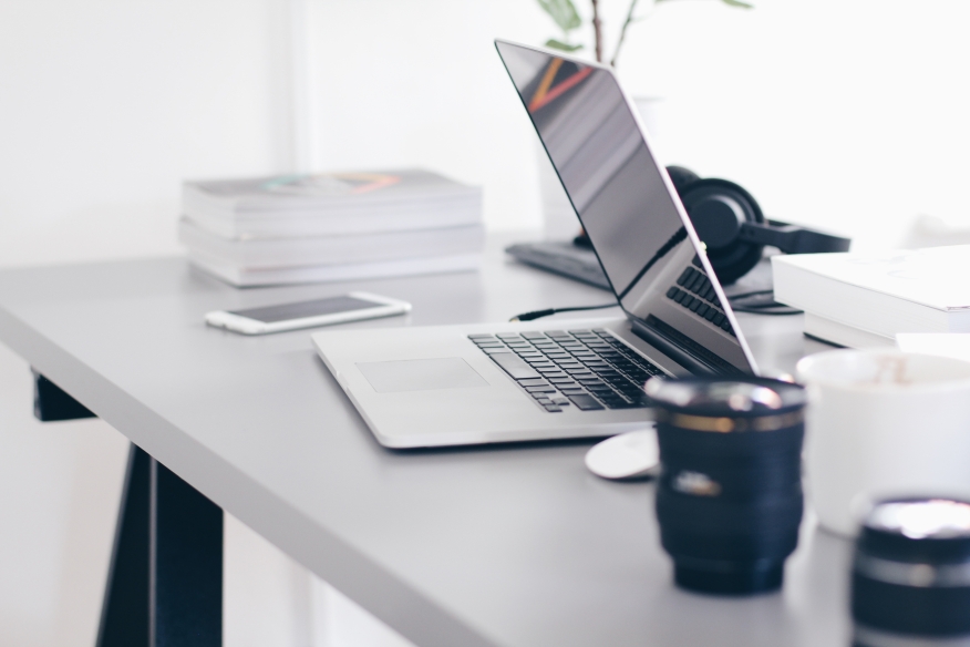 Laptop on a desk with a coffee cup and pens.