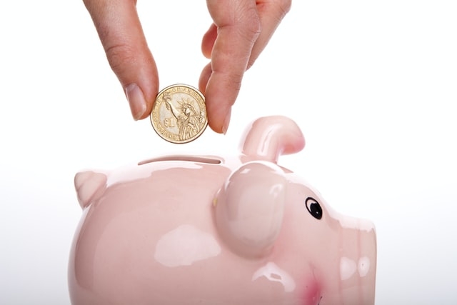 Person putting a gold U.S. dollar coin into a piggy bank.