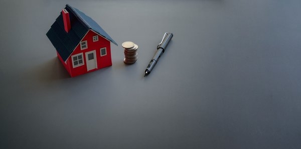 Model house next to a stack of coins and a pen.