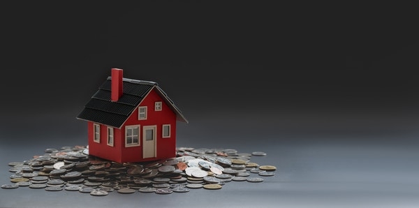A model of a house atop a pile of coins.