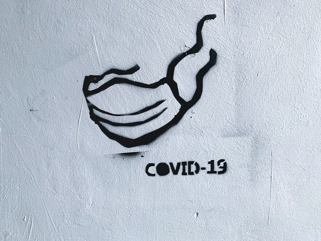 Photo of a spray painted masked and the word COVID-19.