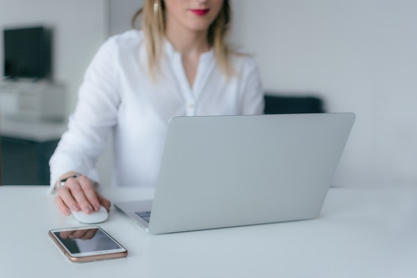 Photo of a woman working on her laptop with cell phone nearby.