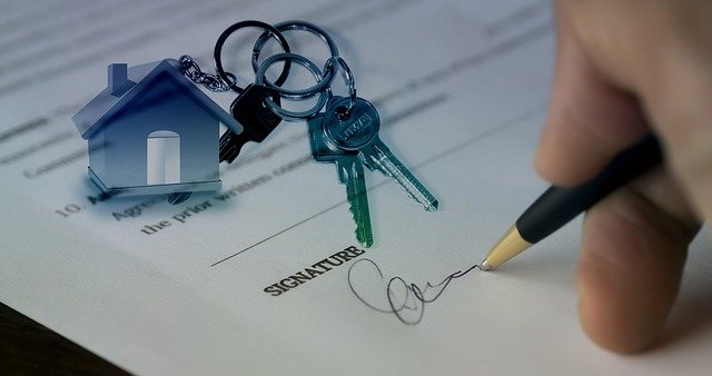 Mini house and keys overlay on person signing a contract. 