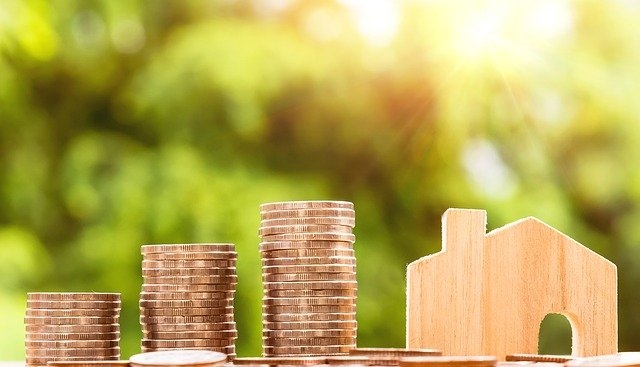 Photo of coins stacking up next to a wooden carving of a house.