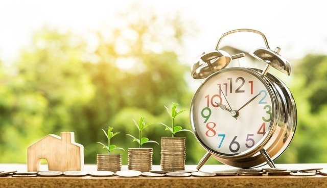 Photo depicting economic and housing growth. Woodcut house, stack of coins and a clock.