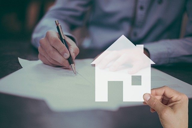 Person signing a mortgage contract with a digital house overlay. 