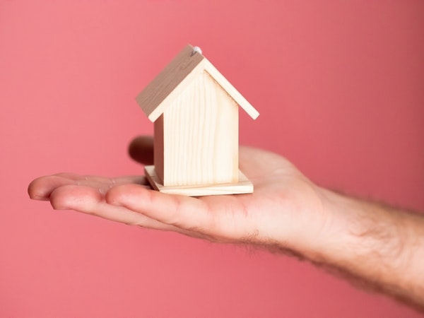 Photo of a wooden house in the palm of a hand. 