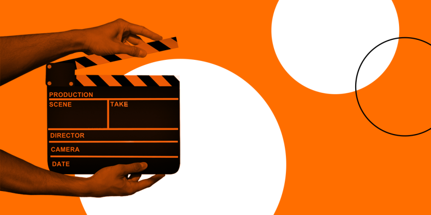 Hands holding a clapperboard, used to cue scenes on video sets, on an orange and white background