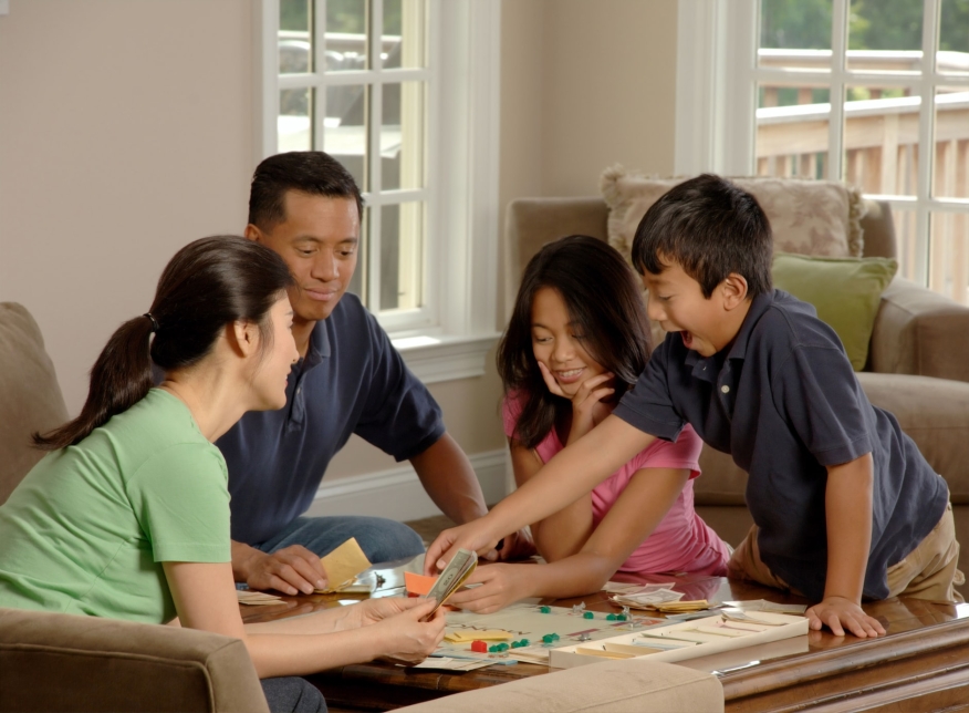An Asian-American family plays Monopoly inside their home.