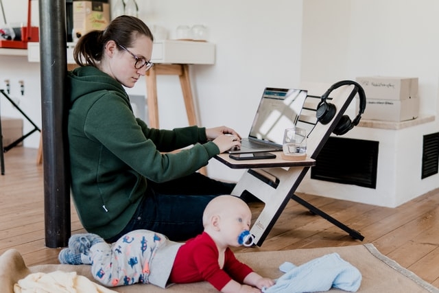 Photo of a mom working from home as an infant lays close by.