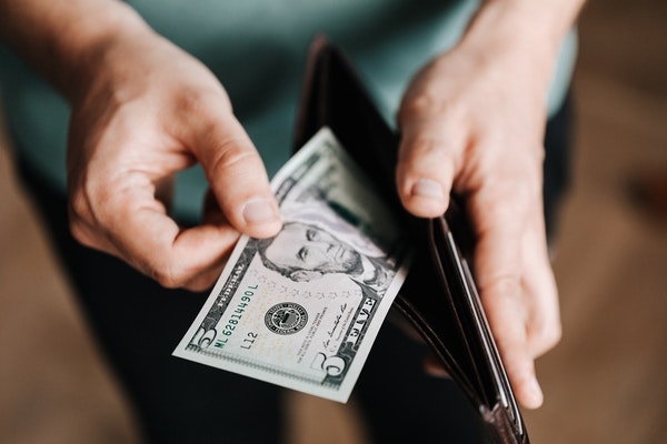 Photo of someone pulling a five dollar bill out of their wallet.