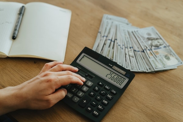 Photo of a person calculating bills with a stack of money on a table.