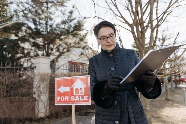 Photo of a realtor standing next to a for sale sign, outside of a home.