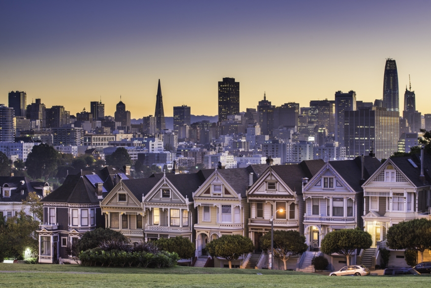 Single family homes line an expensive street in San Francisco with the city in the background. 
