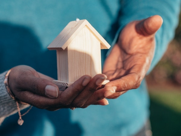 Photo of a small wooden house in the palm of someones hands.