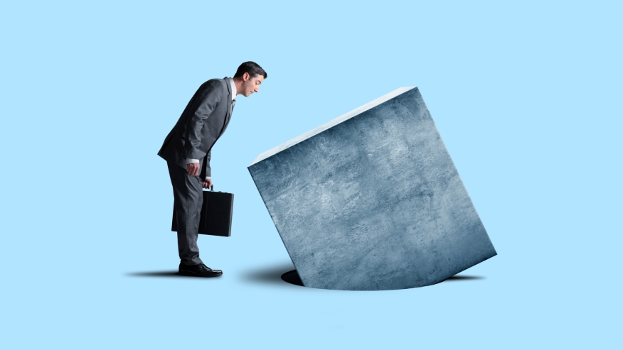 A businessman looks as a large cube does not fit into a hole