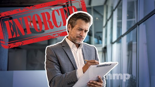 A man holding a clipboard and writing with ENFORCED in the background