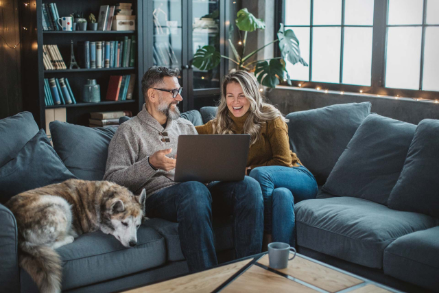 A couple sitting on a sofa with a dog looking at a laptop