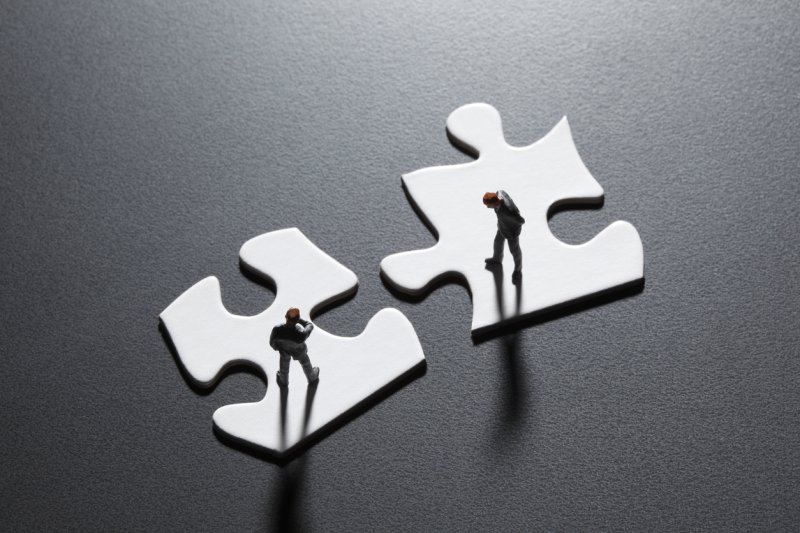 Two miniature businessmen standing on puzzle pieces. 
