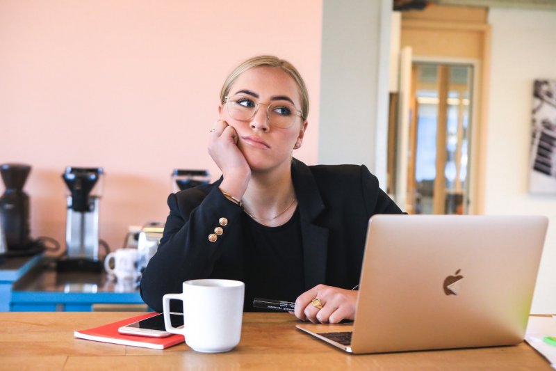 A woman in a suit pouts in front of her laptop, apparently bored. 