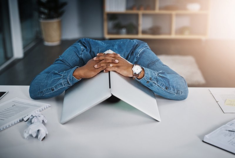 A man covers his head with his laptop, a sign of virtual fatigue.