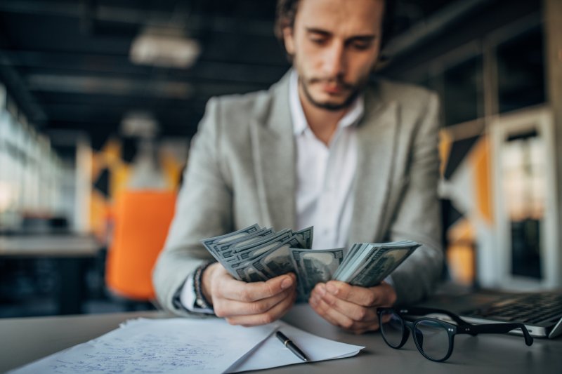 A businessman counts money at his desk, thinking deeply.