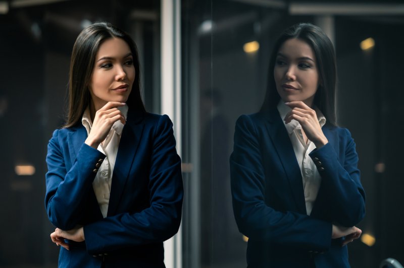 A businesswoman views her reflection in a glass window with a satisfied look. 