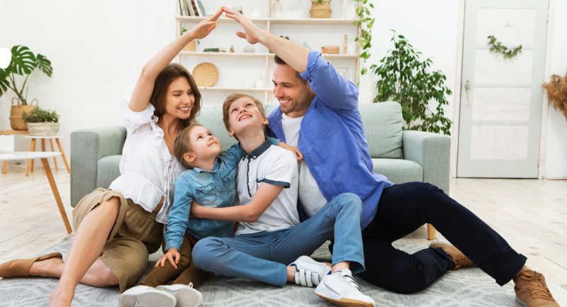 A young family sits together on the floor of their living room