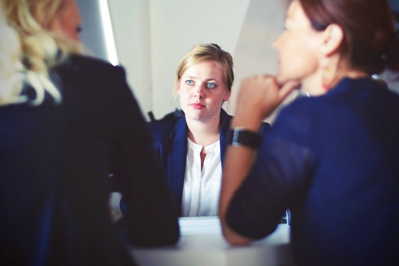 A businesswoman sits across from two others, being interviewed. 