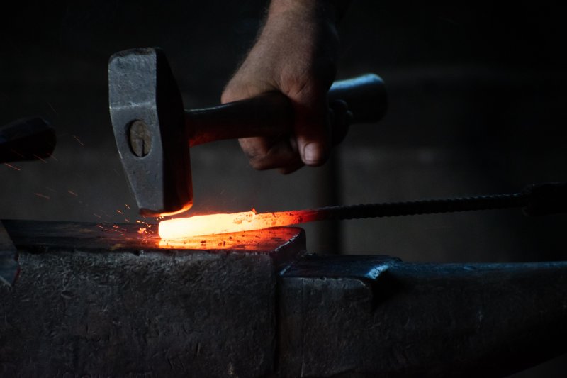 A hammer strikes a glowing hot piece of metal.