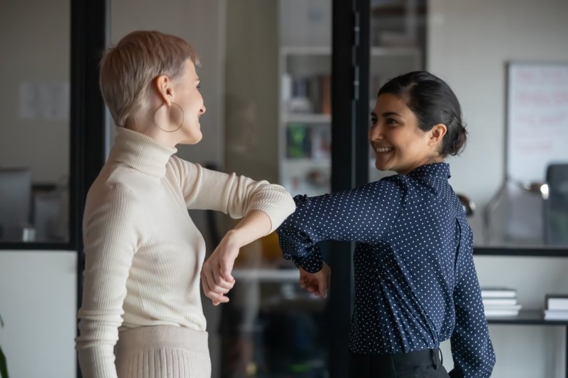 Two women tap elbows, avoiding a handshake.