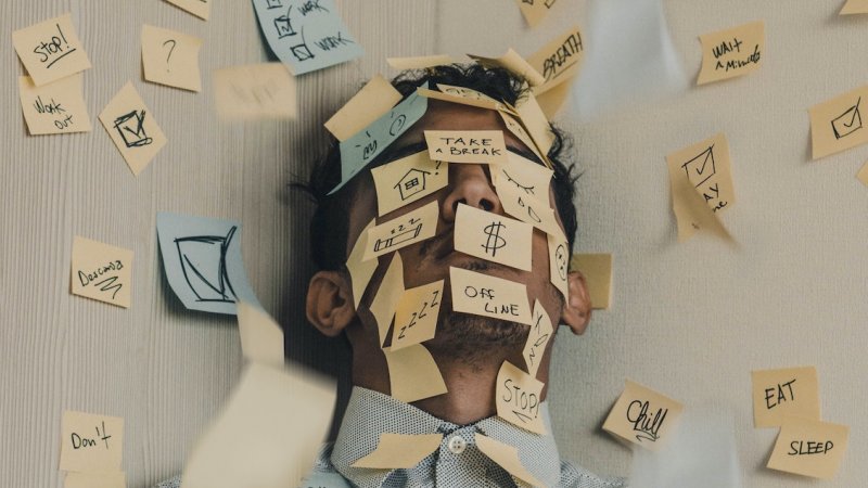 A man's tired face is covered with sticky notes reminding him to relax.