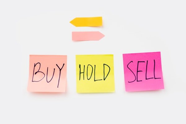 Three sticky notes with the words buy, hold, sell and arrows pointing to opposite sides.