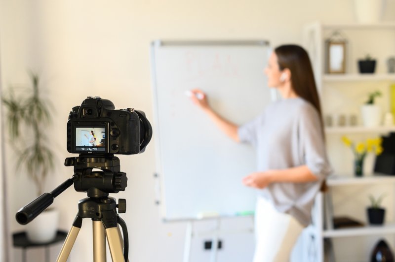 A woman stands in front of a recording camcorder