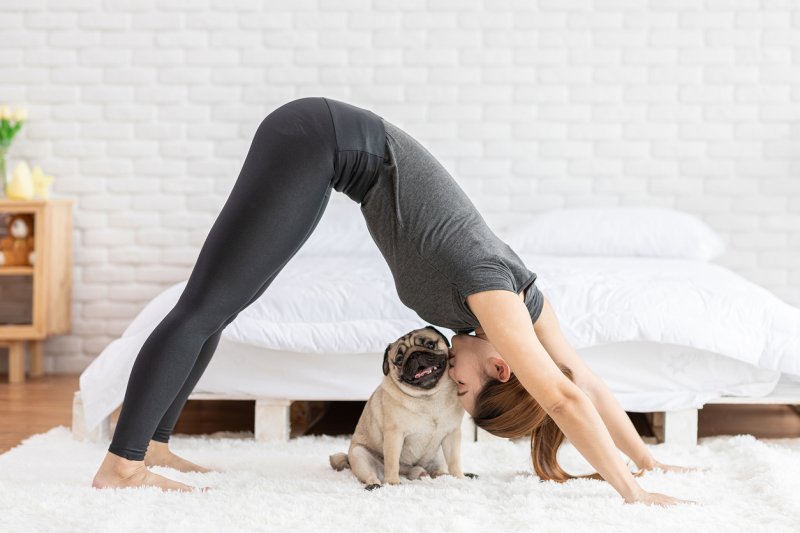 A woman does a yoga pose while kissing her pug.