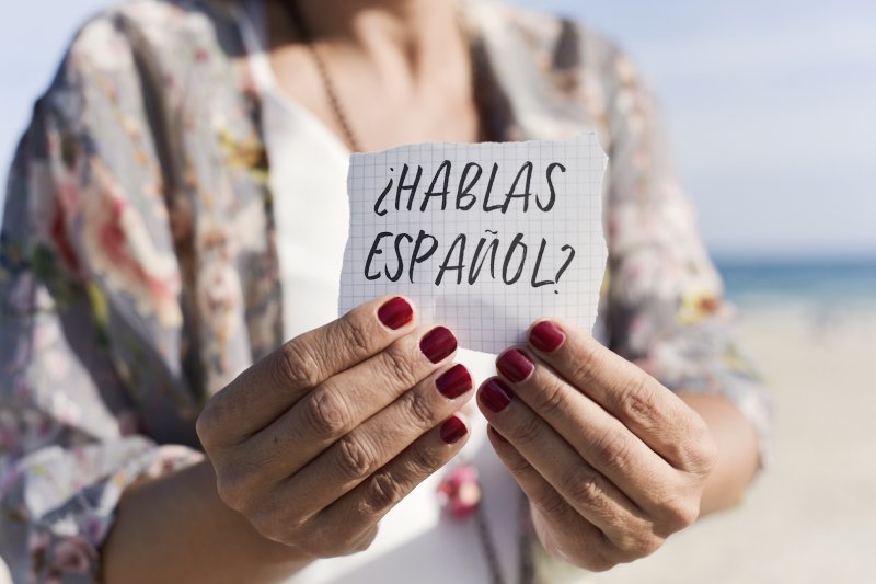 Wrinkled hands hold a sign reading ¿HABLAS ESPAÑOL?