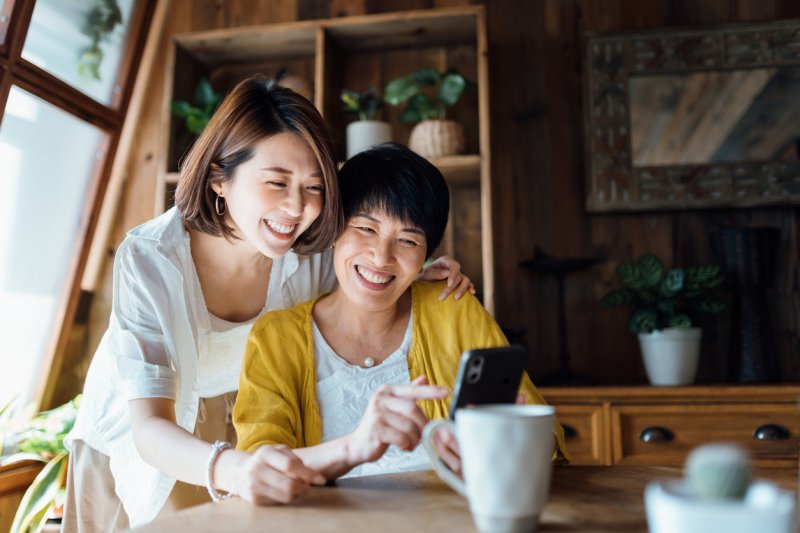 A woman and her mother smile while using a smartphone.