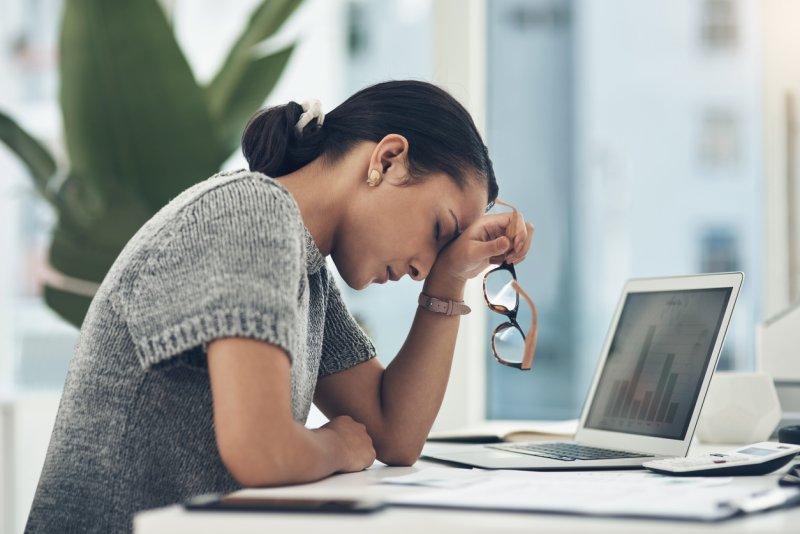 A stressed employee with her head in her hands at her desk. 