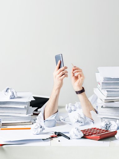 A loan officers arm reach up from beneath a pile of papers and work.